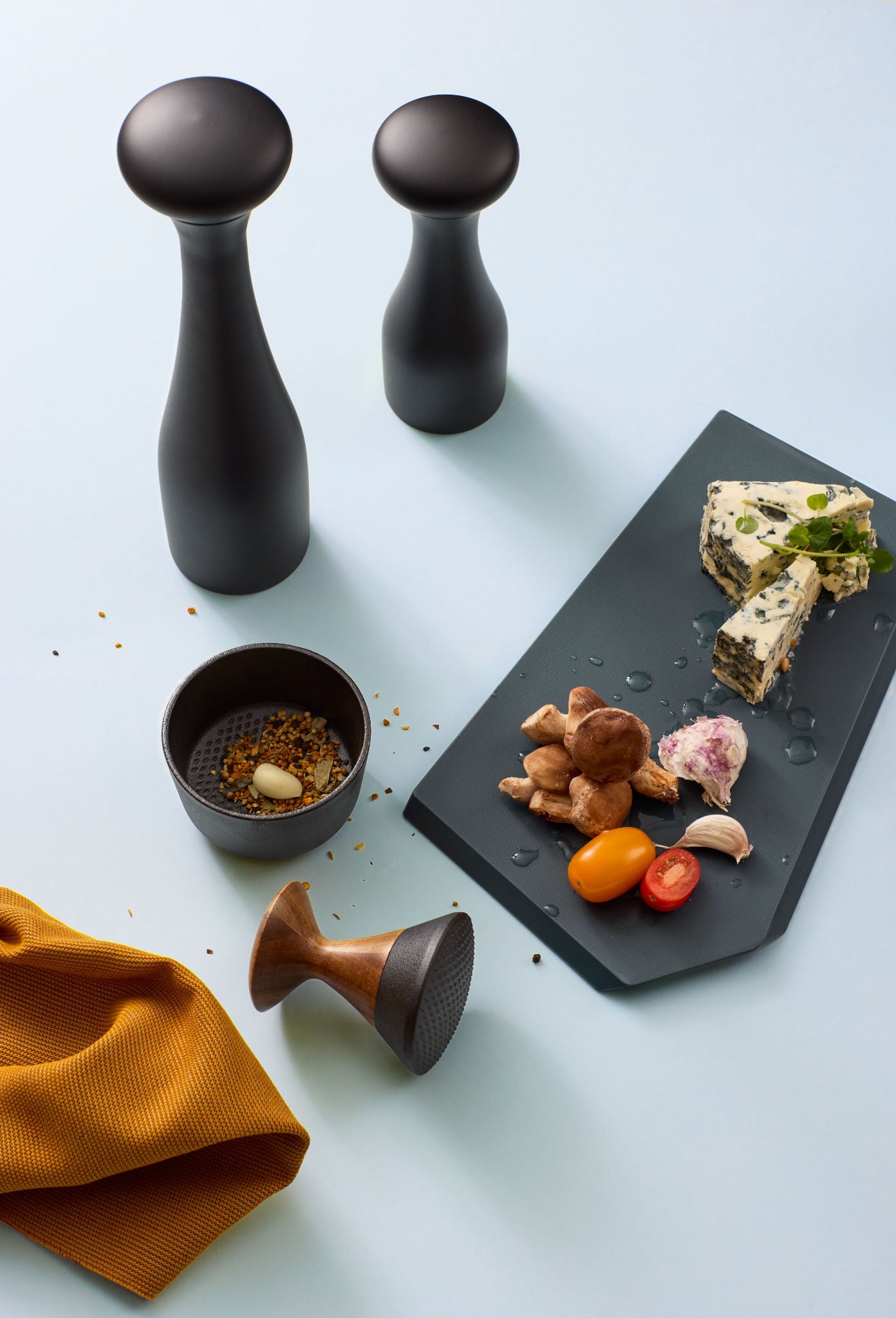 Kiruna Gewürzmörser aus Gusseisen mit Akazienholz-Stößel, frische Zutaten und Pfeffermühle auf heller Küchenoberfläche