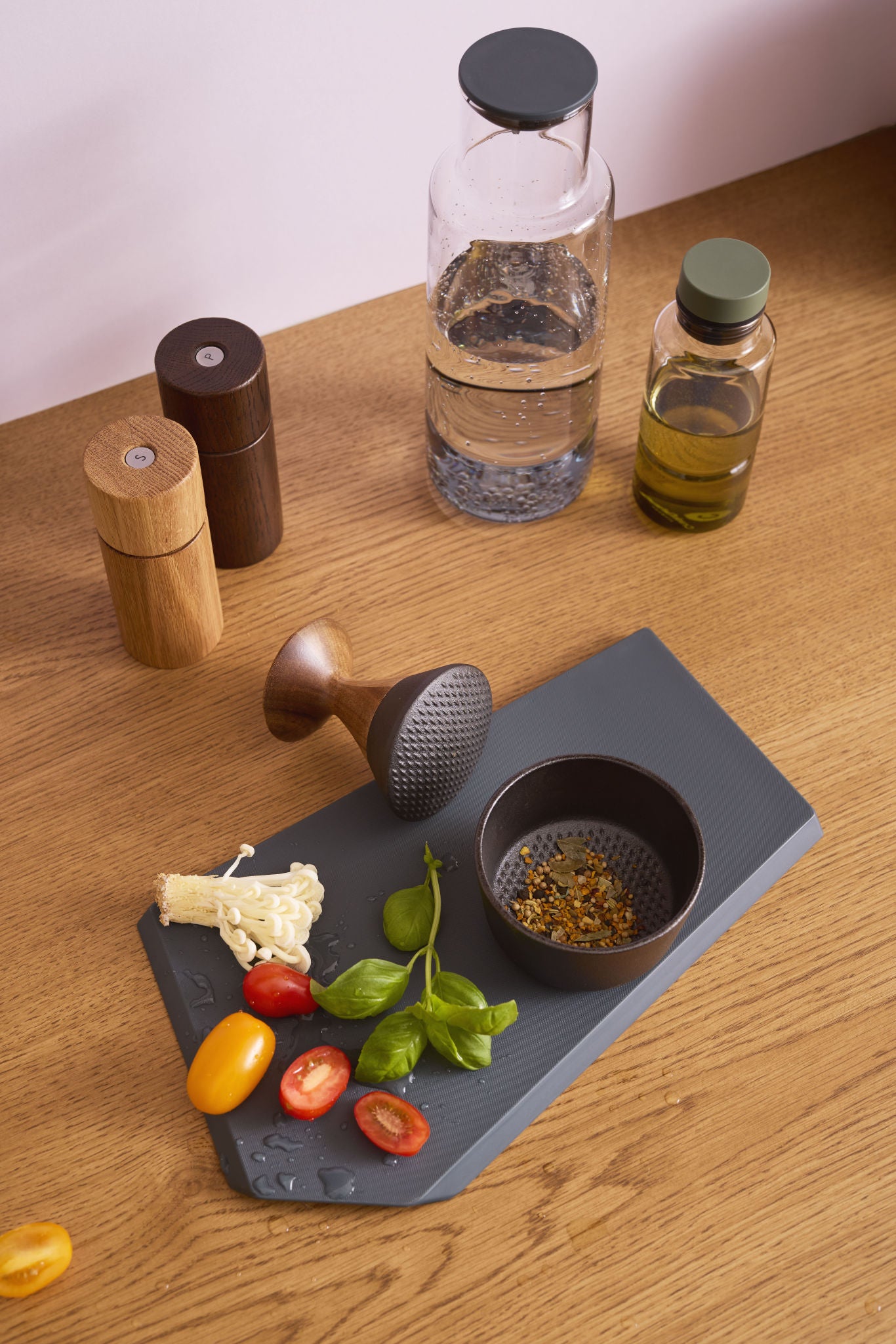 Kiruna Gewürzmörser aus Gusseisen mit Akazienholz-Stößel, mit frischen Zutaten, Wasserflasche, Ölflasche und Pfeffermühlen auf Küchenarbeitsplatte aus Holz