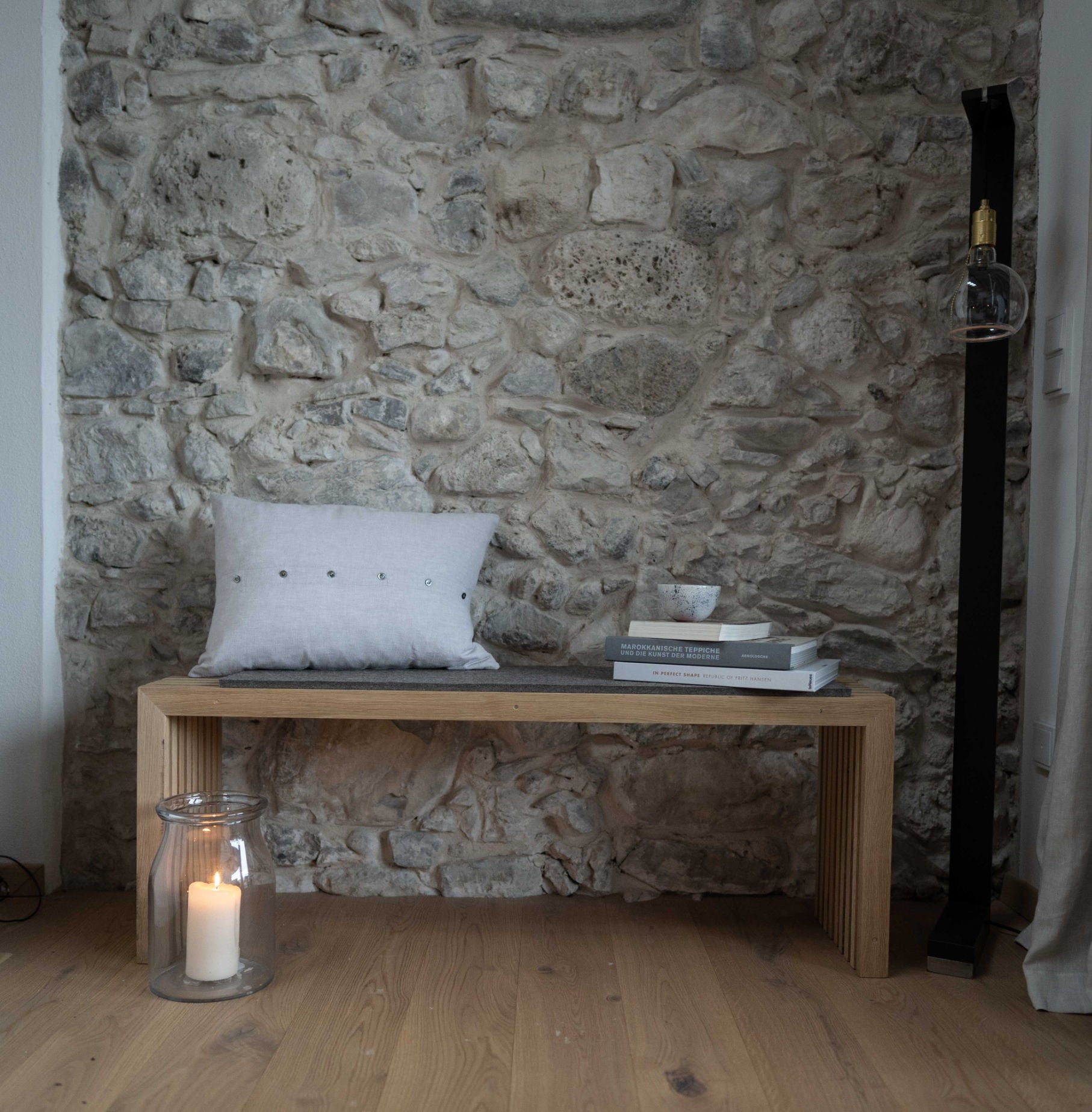 Bank aus Eichenlamellen von Raumgestalt mit Filzauflage ud Kissen im Eingangsbereich